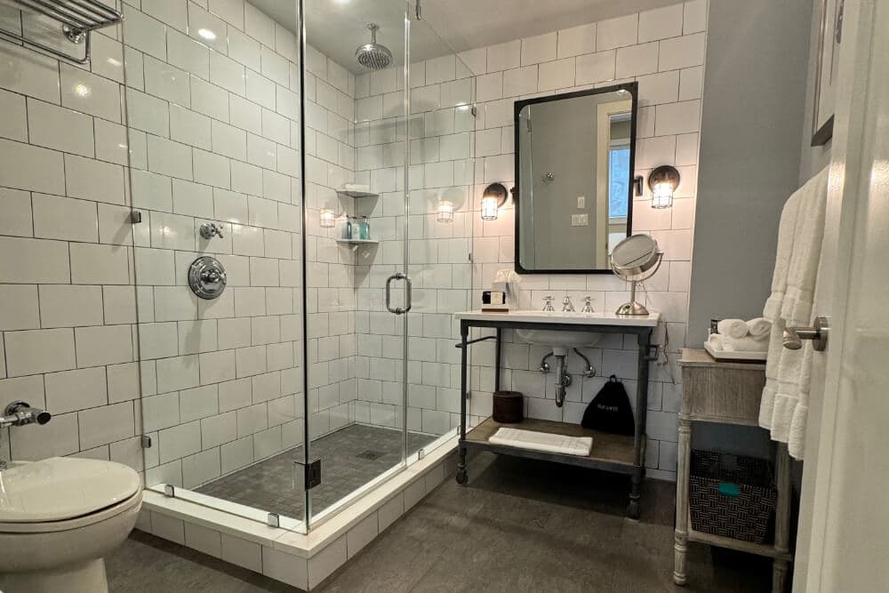 A chic bathroom with a walk in shower with clear glass sides, a vanity with sink and makeup mirror
