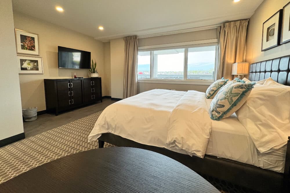 A bedroom with a bed with white bedding and blue starfish throw pillows, a dresser, flat screen TV, and table.