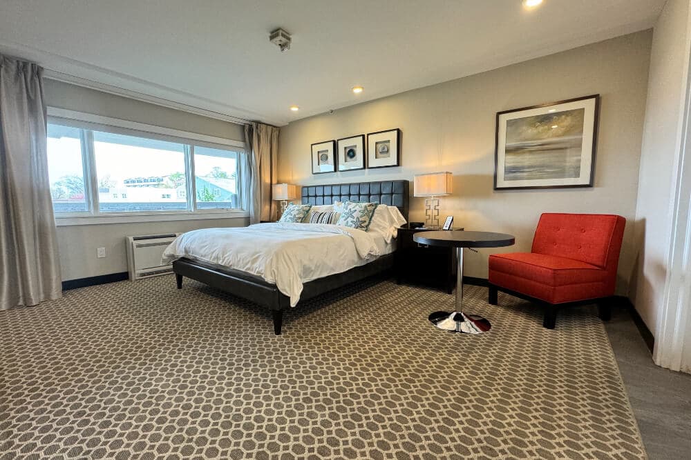 A bedroom with a bed with white bedding and blue starfish throw pillows, a table, and a plush red chair.
