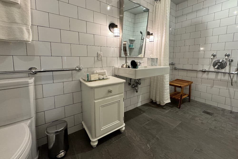 A bathroom that's handicapped accessible with a roll in shower, a low sink, and toilet, with handrails throughout the bathroom.