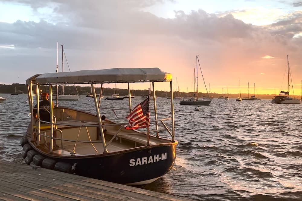 Man in blue shirt and red hat piloting a water taxi boat.