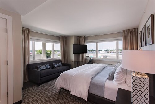 A bedroom with a bed, a sofa, and table, chair and flat screen TV in the corner.