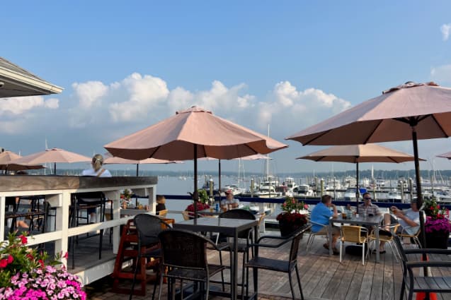 People dining at tables under umbrellas on a waterfront dock