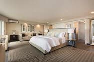 A spacious bedroom with a king bed, side tables with lamps on either side, a sofa and separate sitting area with table and chairs.